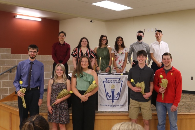 Lamoni National Honor Society induction, NHS members standing in two rows - back row on stage front row on floor in front of stage. New members holding flowers.